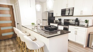 A modern kitchen with white cabinets, a central island with bar stools, stainless steel appliances, and pendant lighting. - Fort Worth 2BR/2BA Home w/ Pool + Games | Sleeps 6 (Fort Worth)