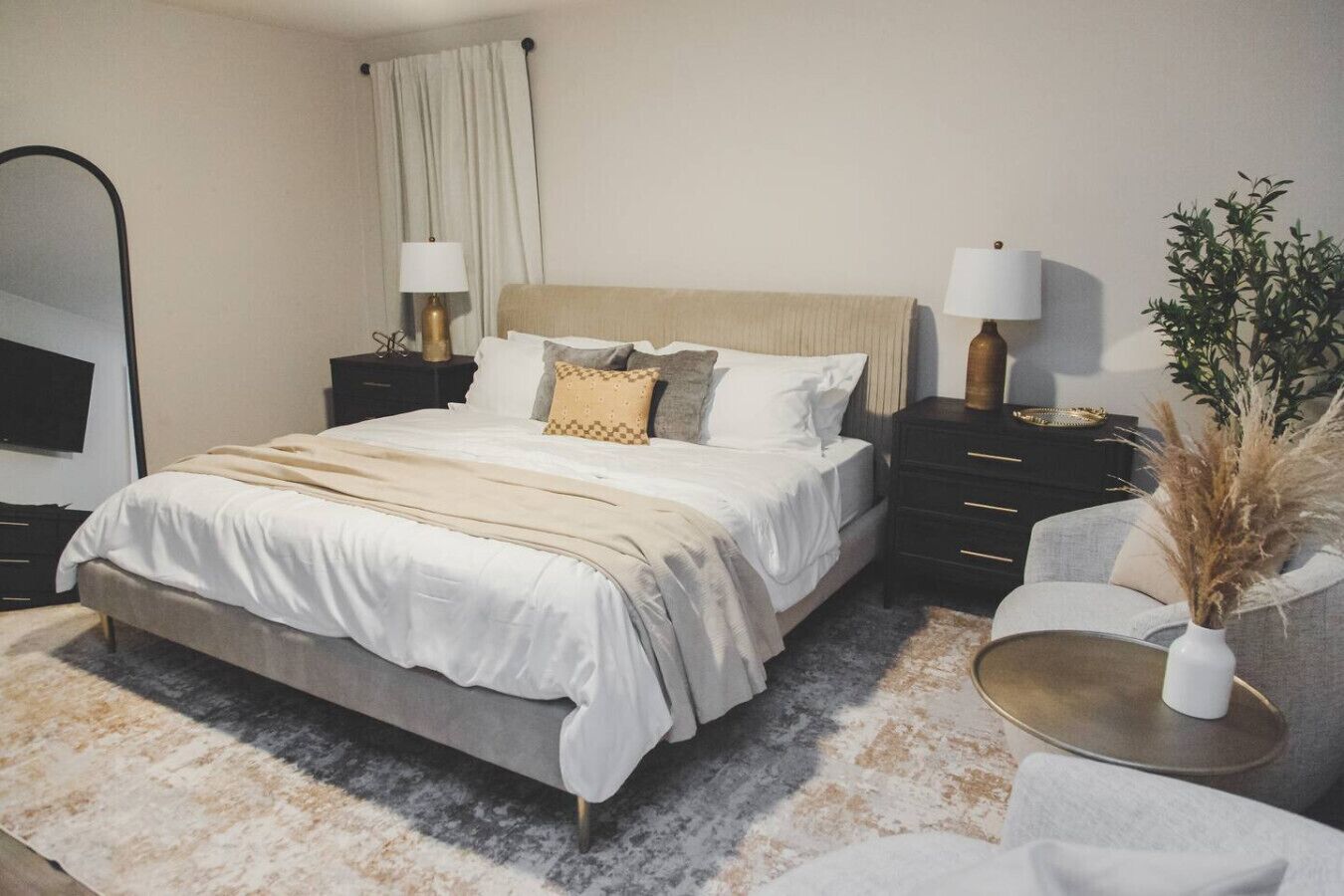 Un dormitorio moderno con una cama grande, mesitas de noche, un espejo y una planta decorativa.