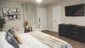A bedroom with a bed, two chairs, a dresser, a TV, and a painting on the wall. - Fort Worth 2BR/2BA Home w/ Pool + Games | Sleeps 6 (Fort Worth)