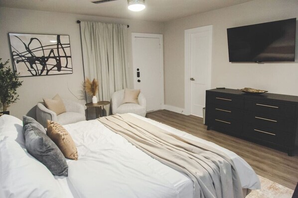 Une chambre à coucher avec un lit, deux chaises, une commode, un téléviseur et un tableau accroché au mur.