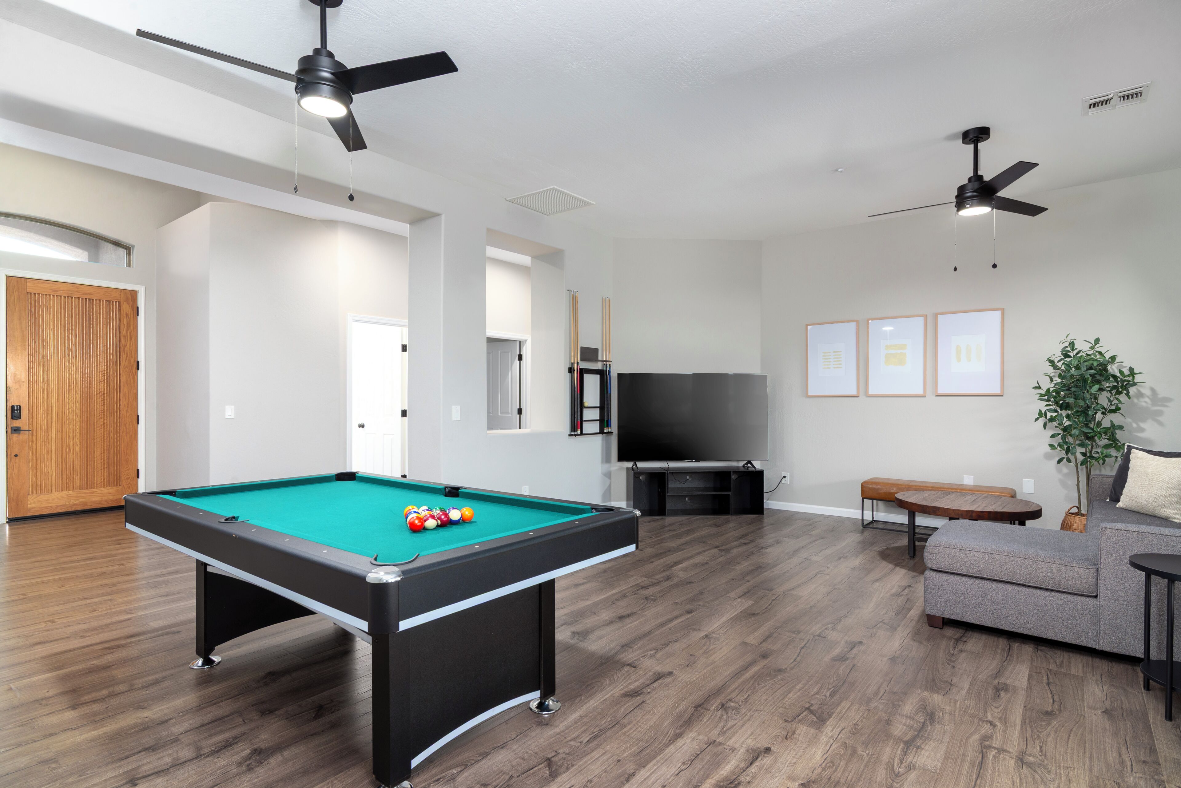 A modern living room with a pool table, ceiling fans, a flat-screen TV, and a sofa.