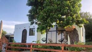 A white building with a large tree in front, a wooden fence, and a signboard. - Casa Playa Rincon Hills Samana (Samaná)