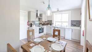 A modern kitchen with white cabinets, a wooden dining table set for four, and a hanging light fixture. - Spacious country suite located at Lonan Country House & Gardens in Scotland! (Taynuilt)
