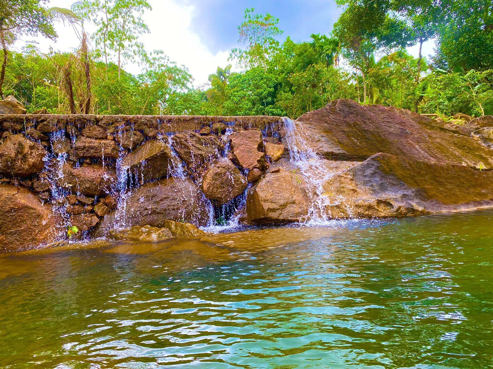 Une cascade d’eau qui dévale des rochers pour se jeter dans une rivière paisible, le tout entouré d’une végétation luxuriante.