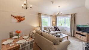 A living room with a sofa, a dining table set for four, a TV, and a painting of a cow on the wall.