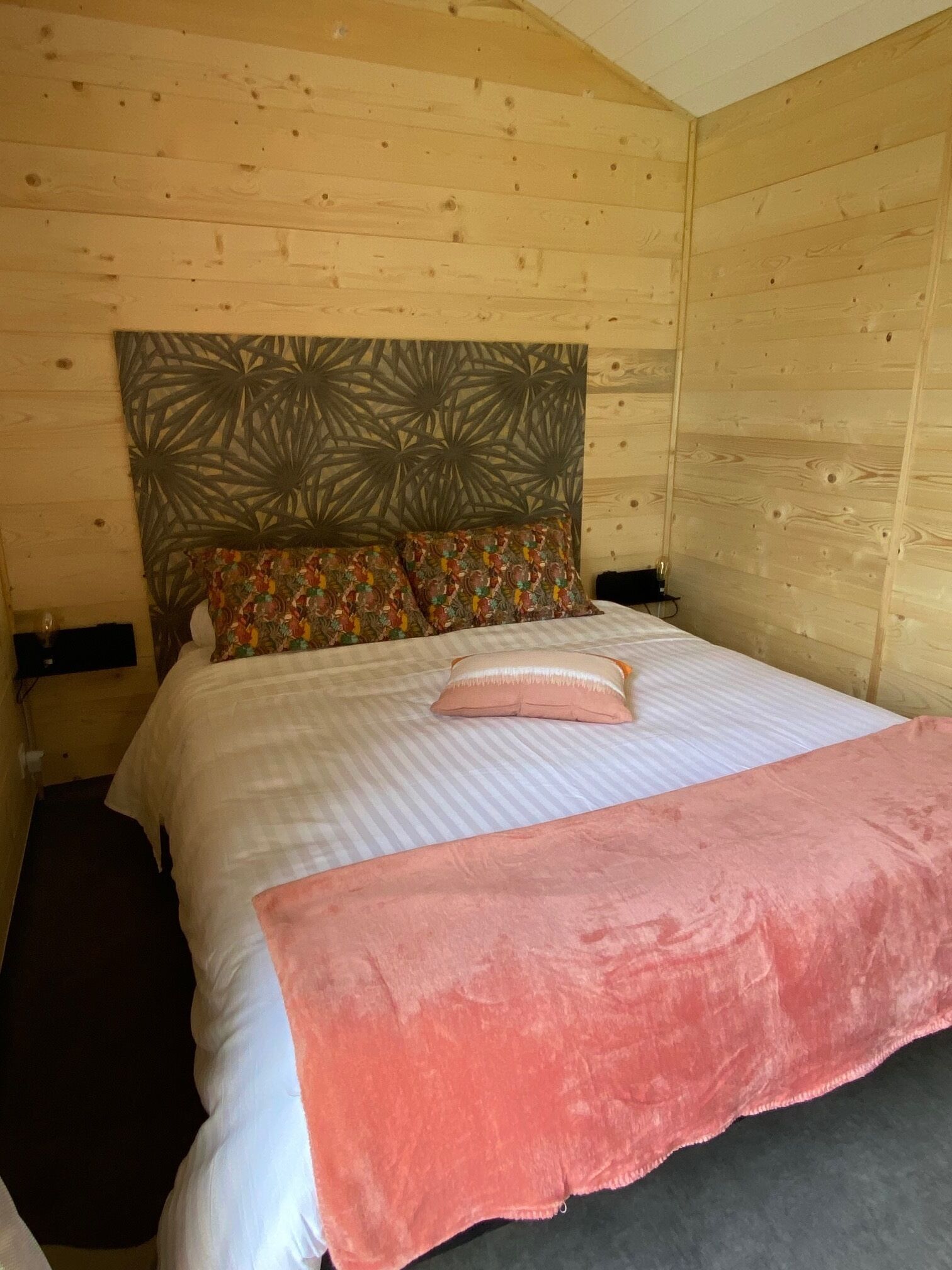 Una habitación de cabaña de madera con una cama, un cabecero con un diseño geométrico y una manta rosa.