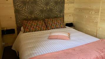 Una habitación de cabaña de madera con una cama, un cabecero con un diseño geométrico y una manta rosa.