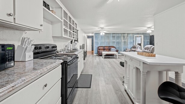 A modern kitchen with white cabinetry, a stove, and a microwave. There is a dining area with a white table and chairs, and a living room with a couch and a TV. - Peaceful 3-bedroom house in Valliant! Close to International Paper and PineCreek (Valliant)