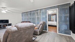 A modern living room with a flat-screen TV, leather recliners, a ceiling fan, and a sliding glass door leading to a bedroom. - Peaceful 3-bedroom house in Valliant! Close to International Paper and PineCreek (Valliant)