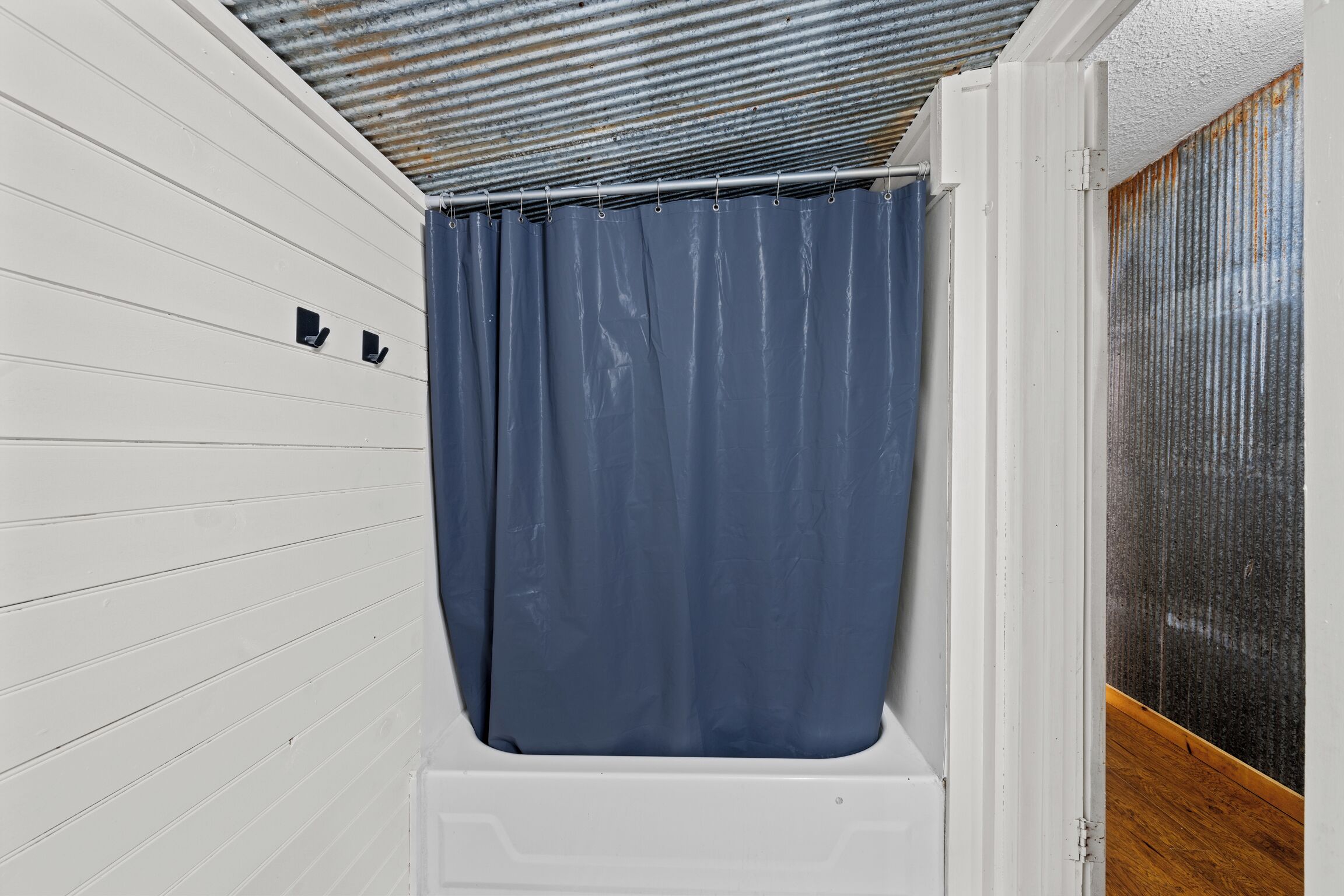 A bathroom with white walls, a blue shower curtain, and a metal ceiling.