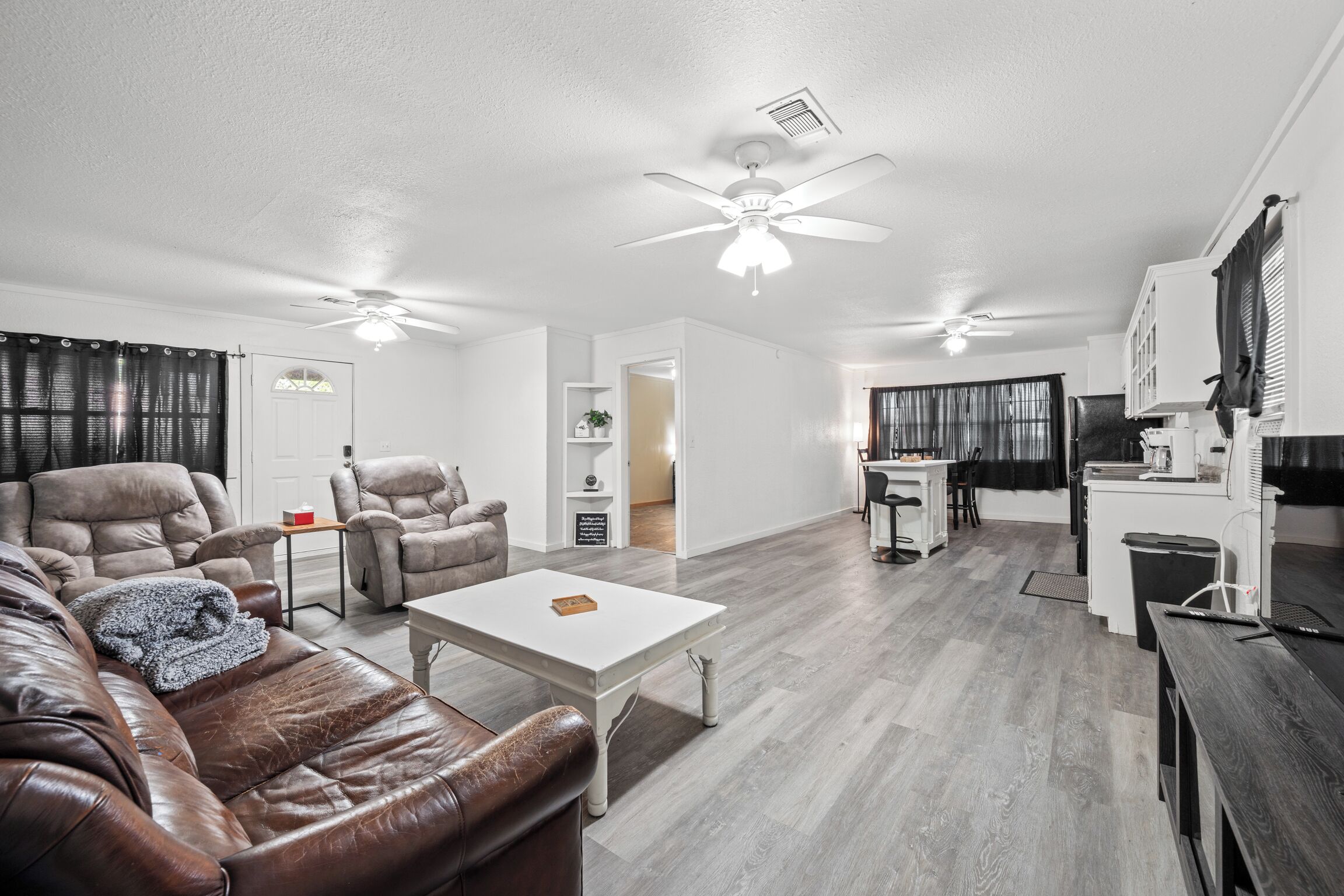 A spacious living area with a brown leather sofa, a white coffee table, and a ceiling fan.