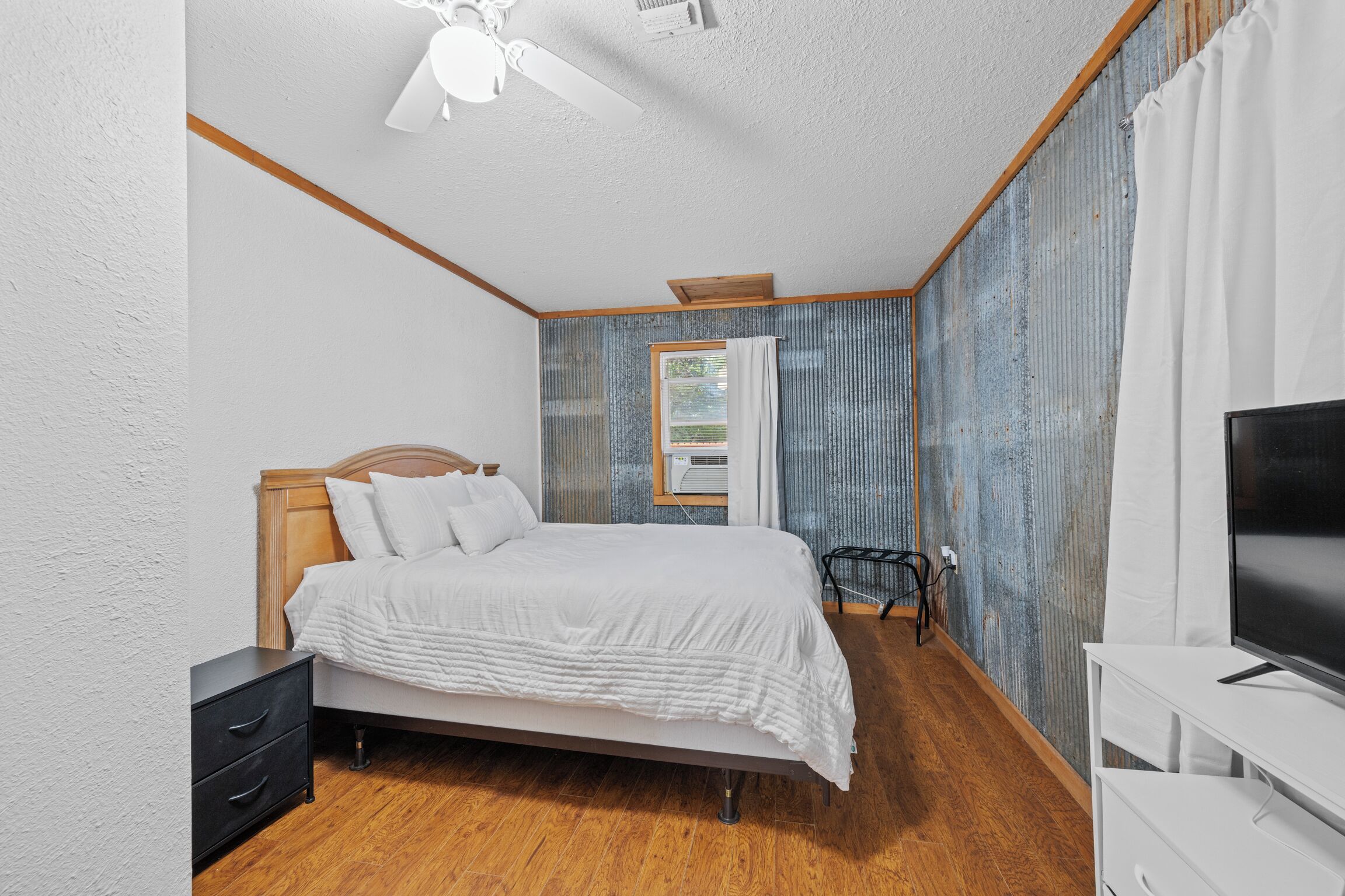 A bedroom with a bed, a TV, a nightstand, and a window with curtains.