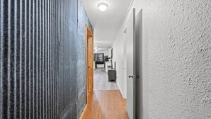 A hallway with a wooden floor, textured walls, and a door leading to a room. - Peaceful 3-bedroom house in Valliant! Close to International Paper and PineCreek (Valliant)