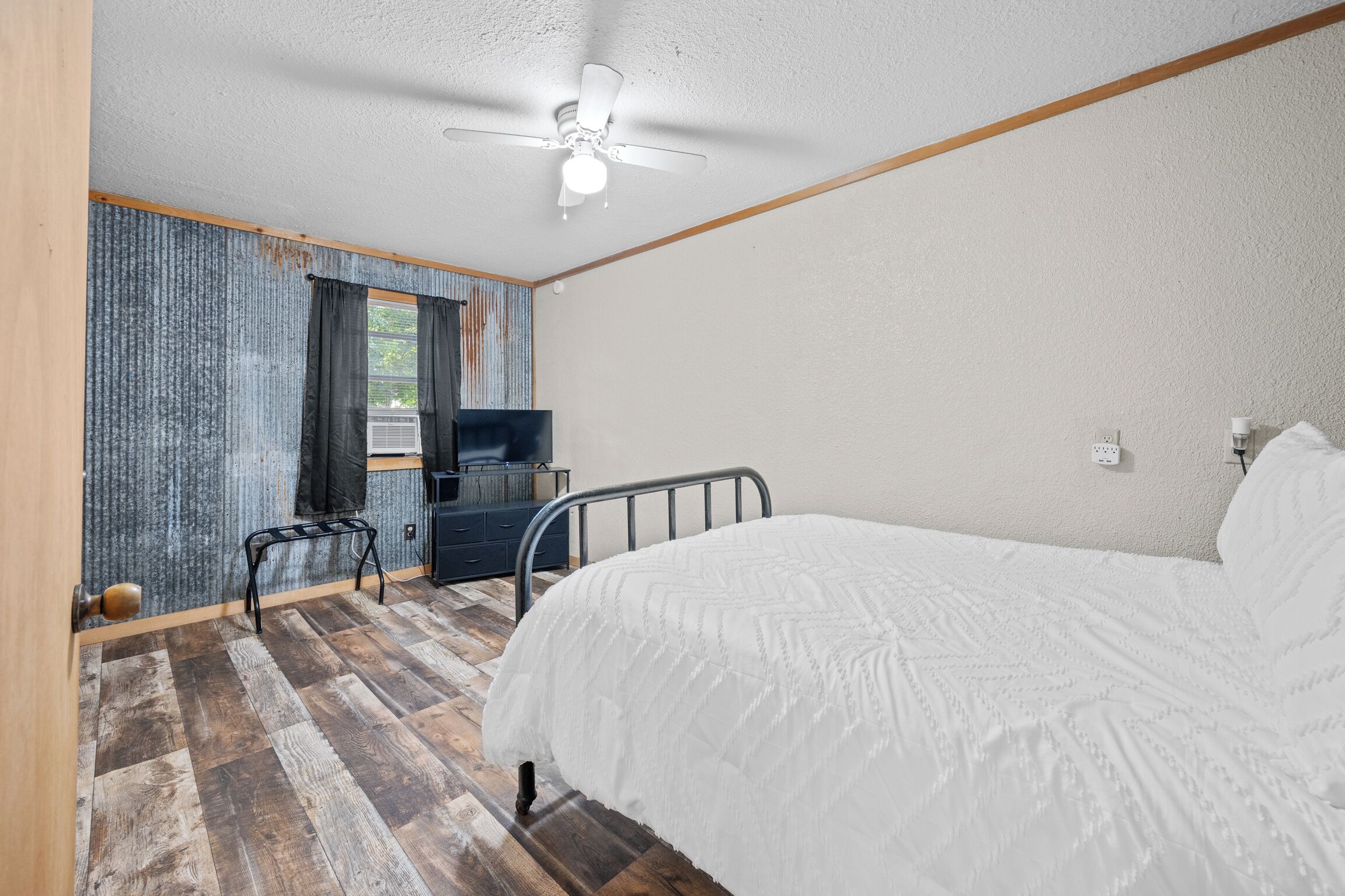 A bedroom with a bed, a ceiling fan, a window with curtains, a desk, and a chair.
