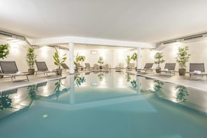 Uma grande piscina interior com espreguiçadeiras e plantas em vasos.