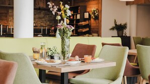 A dining area with a wooden table set for two, surrounded by green chairs. - AlpenParks Hotel & Apartment Alpendorf (Sankt Johann im Pongau)