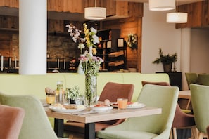 A dining area with a wooden table set for two, surrounded by green chairs. - AlpenParks Hotel & Apartment Alpendorf (Sankt Johann im Pongau)