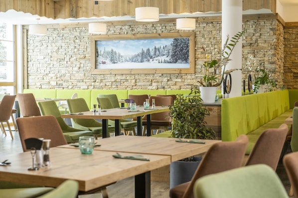 A restaurant with a stone wall, wooden ceiling, and green seating.