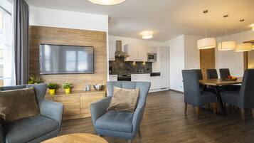 Una sala moderna con televisor de pantalla plana, sofás grises, una mesa de centro de madera y un comedor con mesa y sillas de madera.