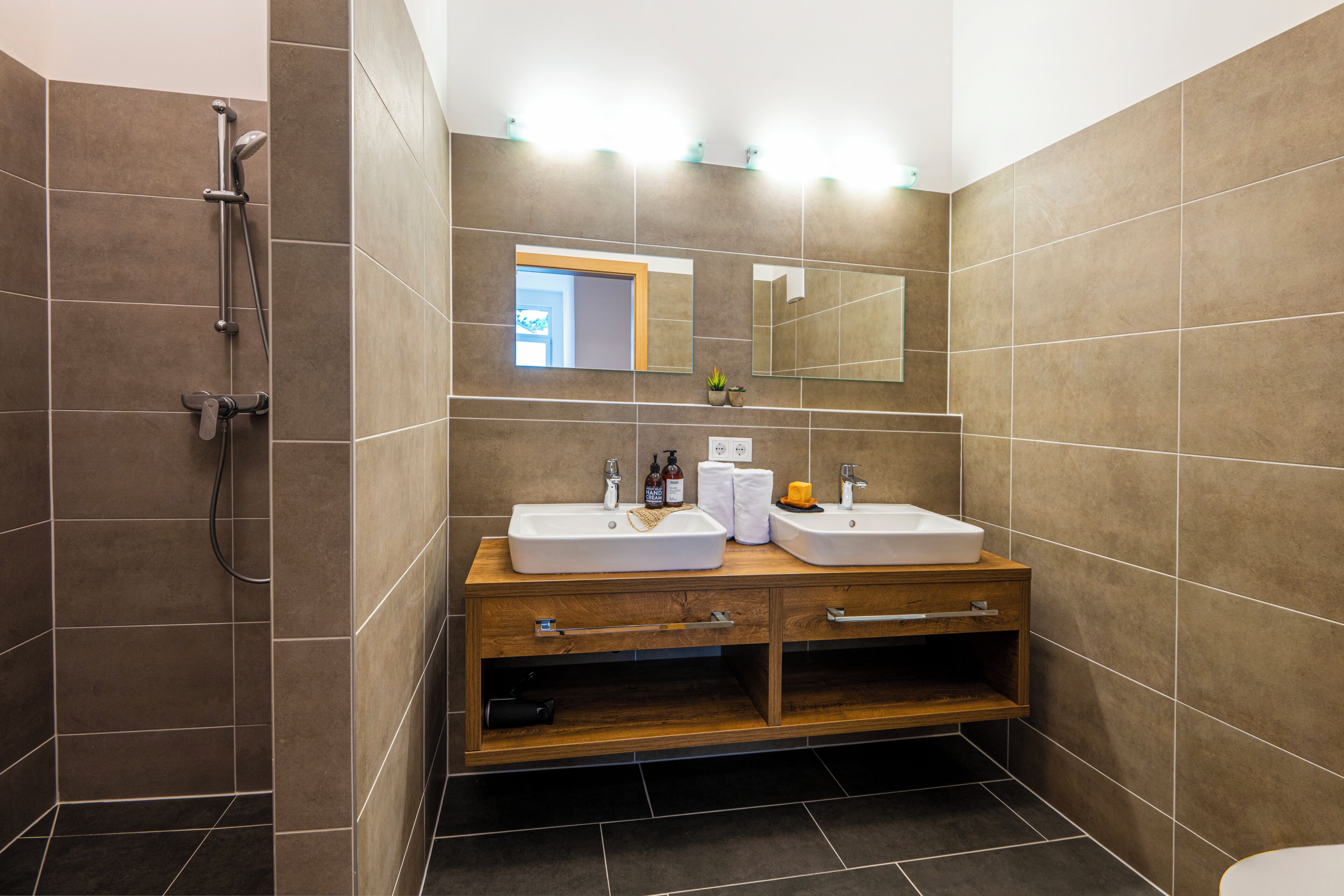 Un baño moderno con dos lavamanos, ducha y tocador de madera.
