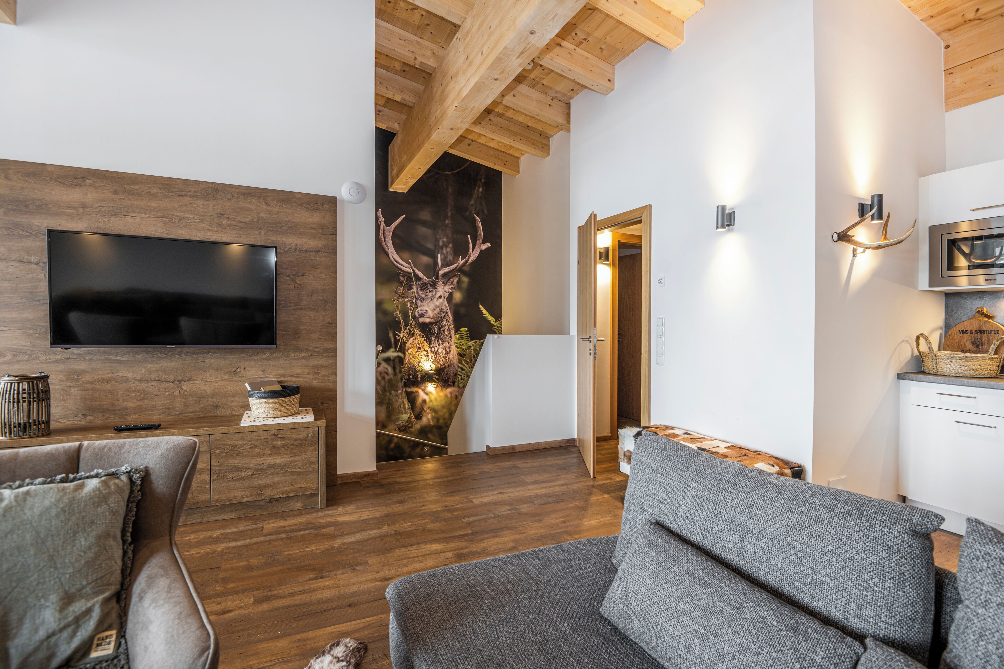 Una sala de estar moderna con una televisión de pantalla plana, piso de madera y una decoración de cuernos de ciervo.