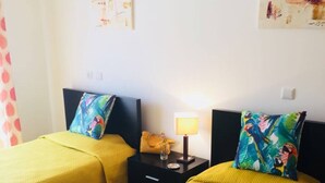 A hotel room with two beds, each with a yellow bedspread and matching pillows. There is a nightstand with a lamp between the beds. - Bright & Spacious 3-Bed Apartment - Pool, Garden, AC, Walk to Beach, Golf 5 Mins (Lagos)