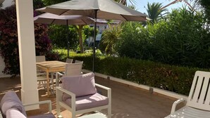 An outdoor patio area with white furniture, including a sofa and chairs, under a large umbrella. - Bright & Spacious 3-Bed Apartment - Pool, Garden, AC, Walk to Beach, Golf 5 Mins (Lagos)