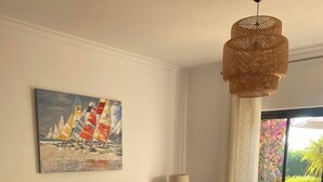 A living room with a beige sofa, a coffee table, and a painting of sailboats on the wall. - Bright & Spacious 3-Bed Apartment - Pool, Garden, AC, Walk to Beach, Golf 5 Mins (Lagos)