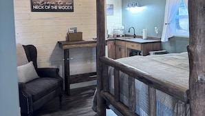 A rustic bedroom with a four-poster bed, a wooden desk, and a chair. A sign on the wall reads "Welcome to our NECK OF THE WOODS." - Wolf Cabin at Glacier Hidden Cabins (Columbia Falls)