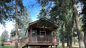 A cabin with a wooden deck and a porch, surrounded by trees. - Wolf Cabin at Glacier Hidden Cabins (Columbia Falls)