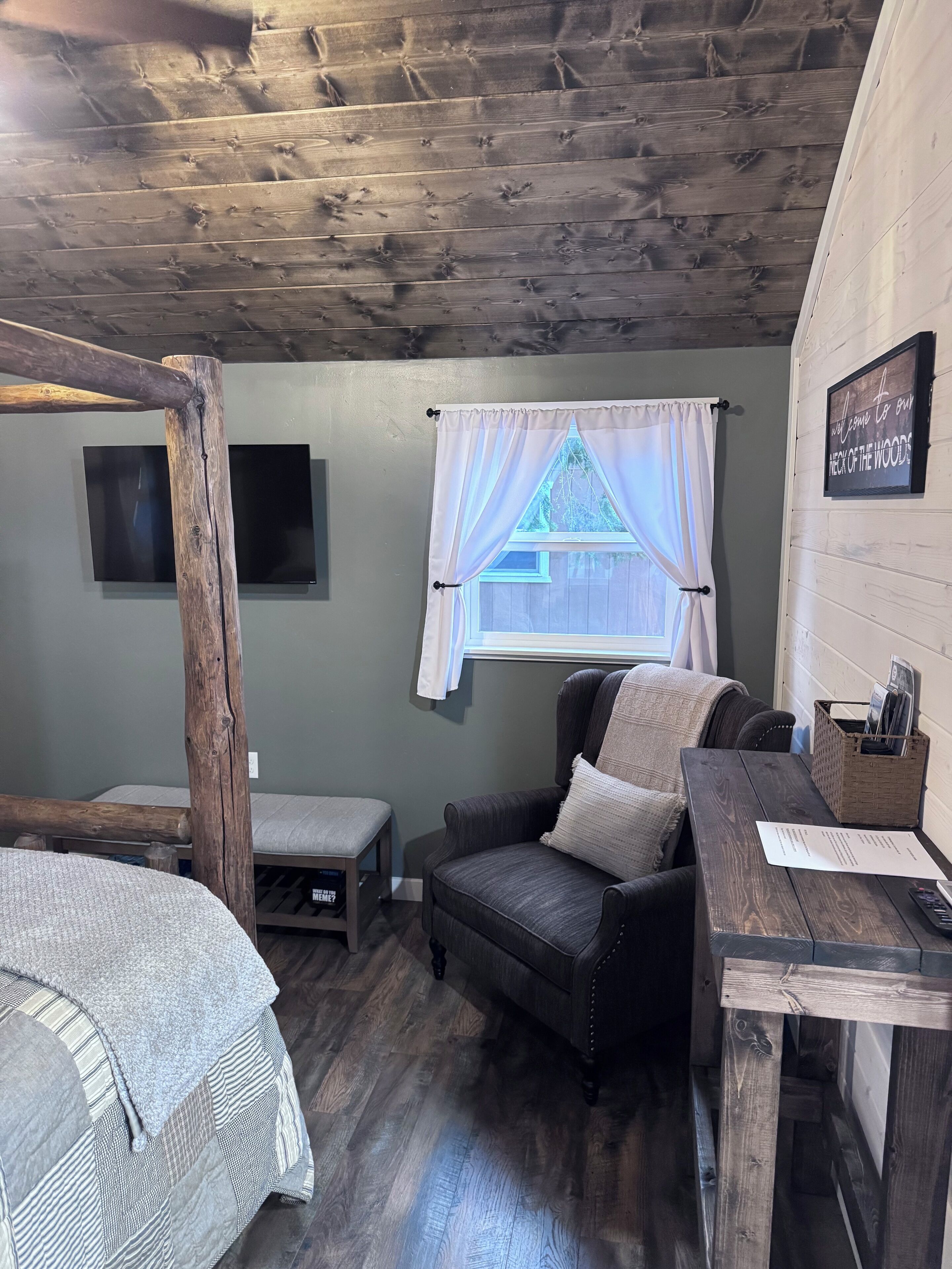 A cozy room with a bed, a chair, a small table, and a window with curtains.