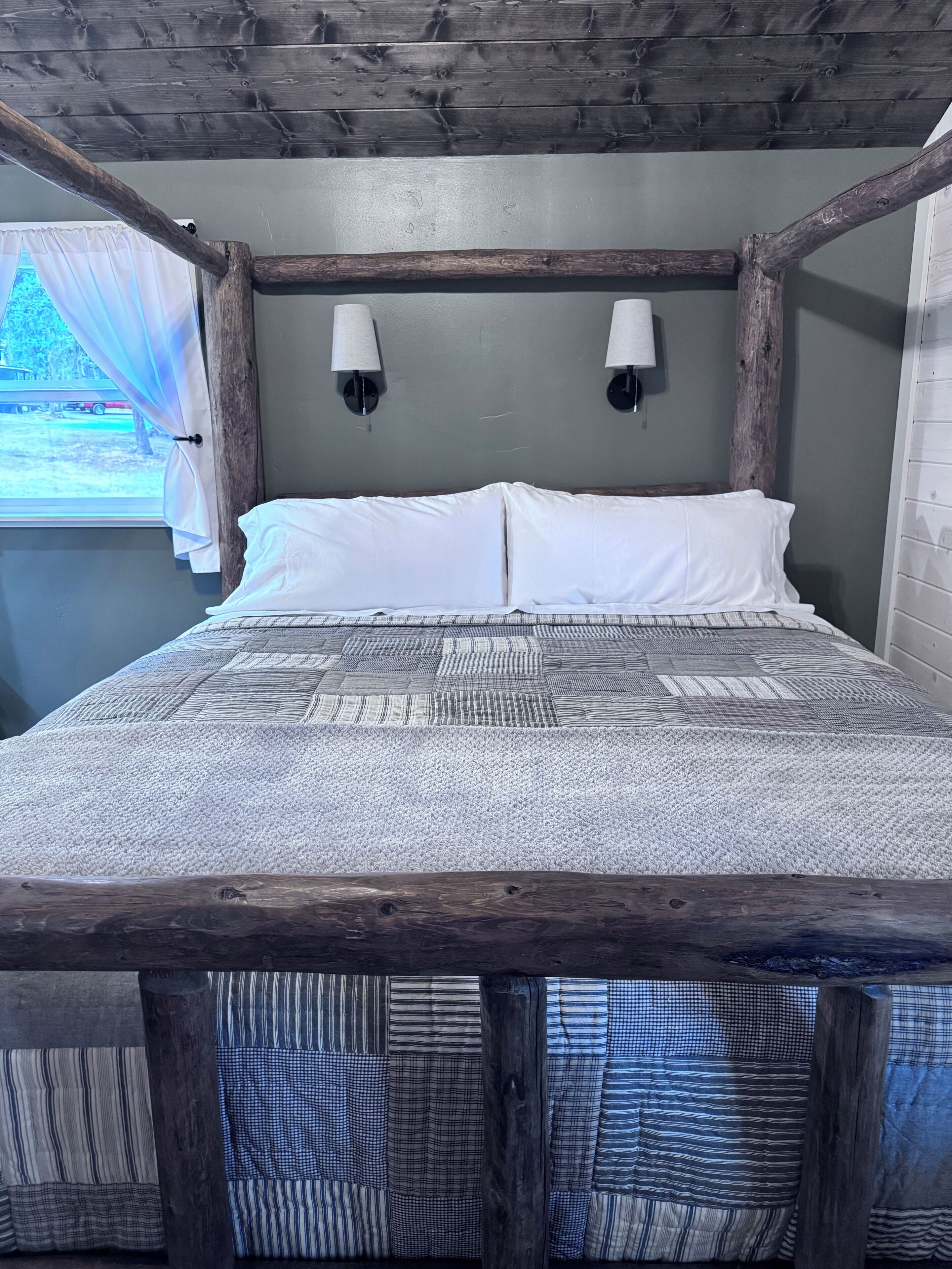 Een bed met een gebedrukte spreidek, twee wandlampen en een rustiek houten hoofdeinde.