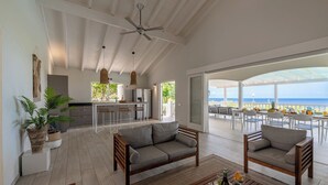 A spacious living area with a sofa, a dining table with chairs, a kitchen area, and a view of the ocean. - Villa Gone Coco - Coral Estate Resort (Sint Willibrordus)