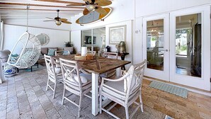 A dining area with a wooden table and white wicker chairs, a ceiling fan, and a hanging chair. - Siesta Key Oasis-Spectacular with heated pool/spa and steps to beach and Village (Siesta Key)