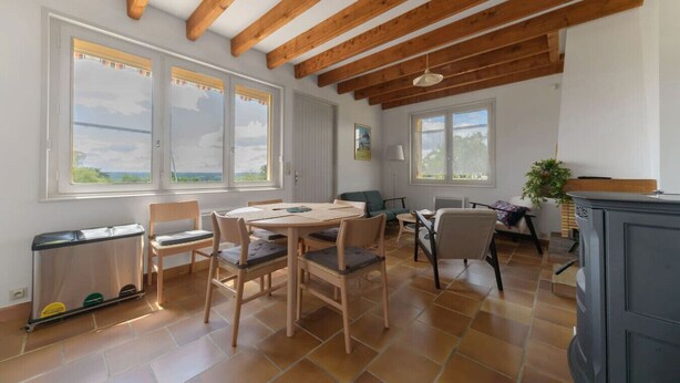 A spacious room with a high ceiling, wooden beams, a dining table with chairs, and large windows offering a view. - Maison Le Berylune - 16bis Rue de Champ des Varennes - Abrest (Abrest)