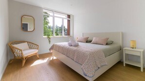Un dormitorio con cama, una silla, una mesita de noche y un ventanal.