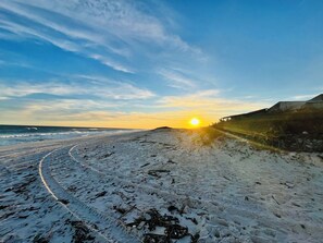 Une plage au coucher du soleil, avec un rivage sablonneux et des vagues.