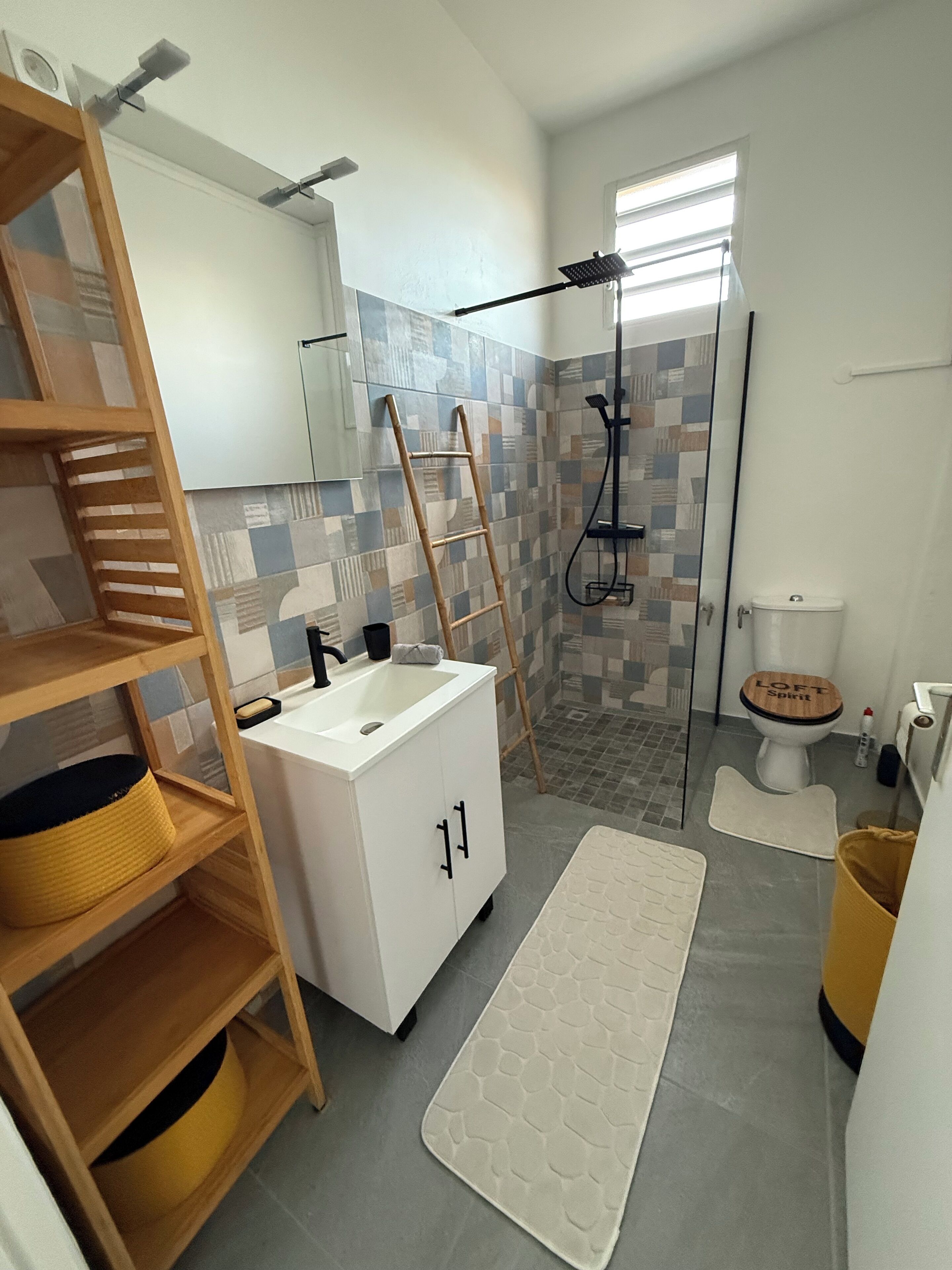 A modern bathroom with a white sink, a wooden toilet, a shower with a glass door, and a wooden ladder.
