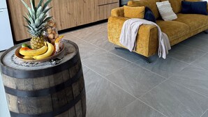 A modern living room with a sofa, a wooden cabinet, a kitchen area with appliances, and a clock on the wall. - Alizé Cap (Sainte-Anne)