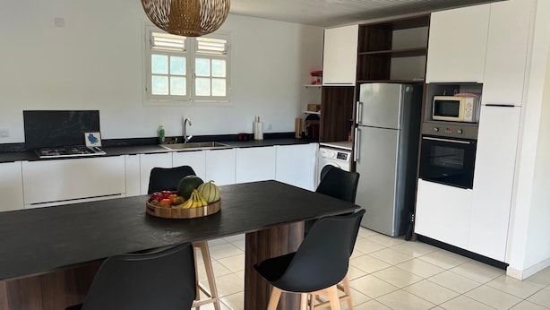 A modern kitchen with a central island, black chairs, and a fruit bowl. - Alizé Cap (Sainte-Anne)