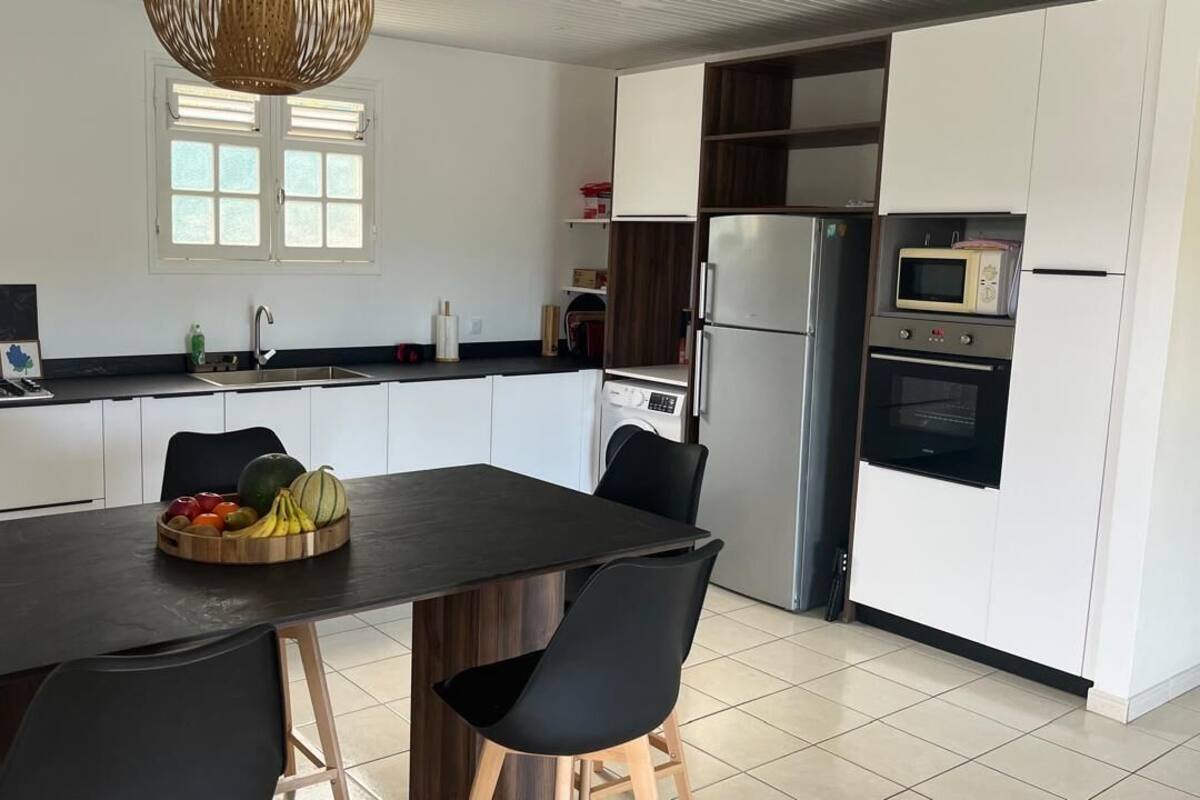 A modern kitchen with a central island, black chairs, and a fruit bowl.