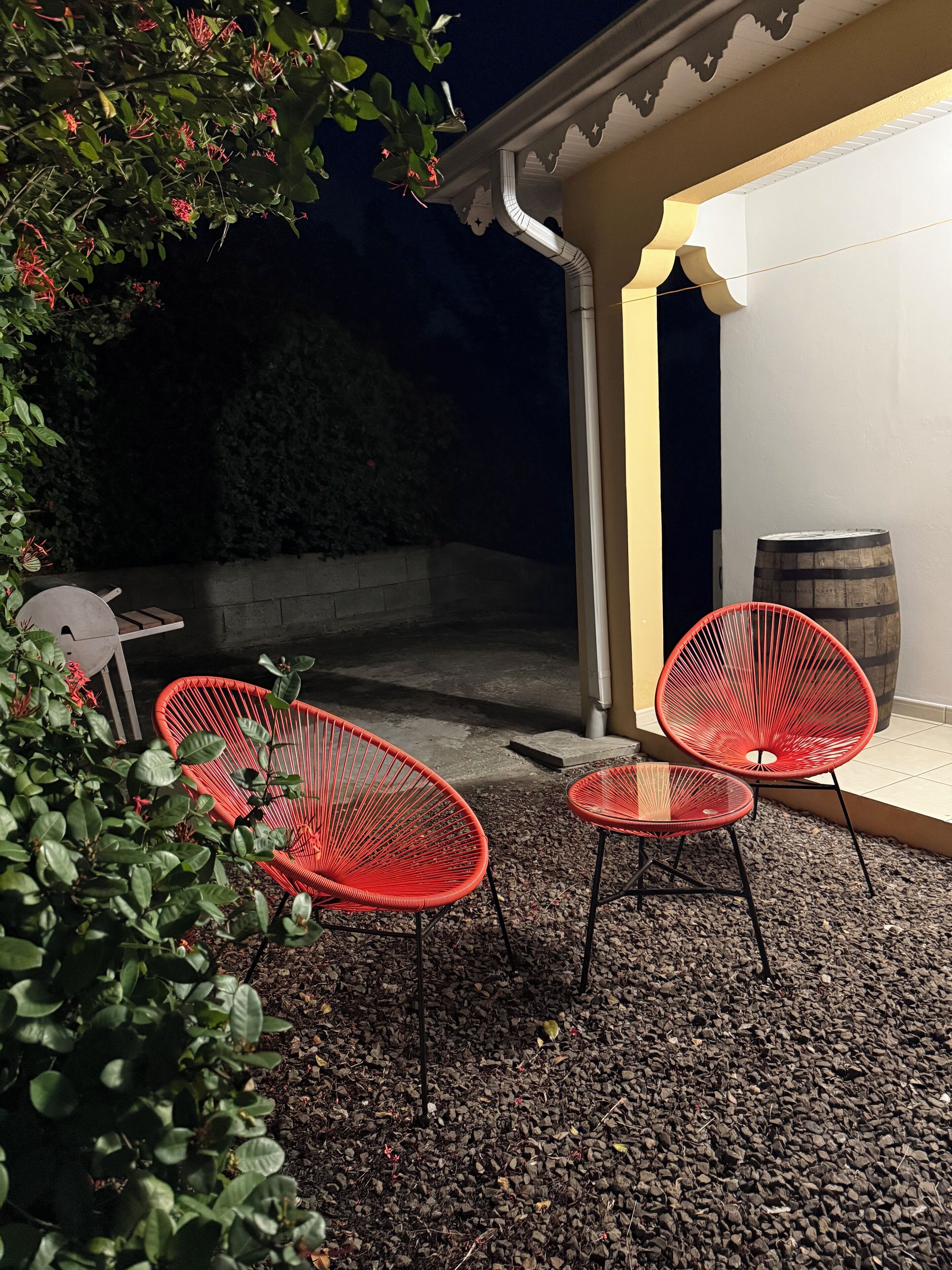 An outdoor patio area with red chairs and a small table, surrounded by gravel and greenery.