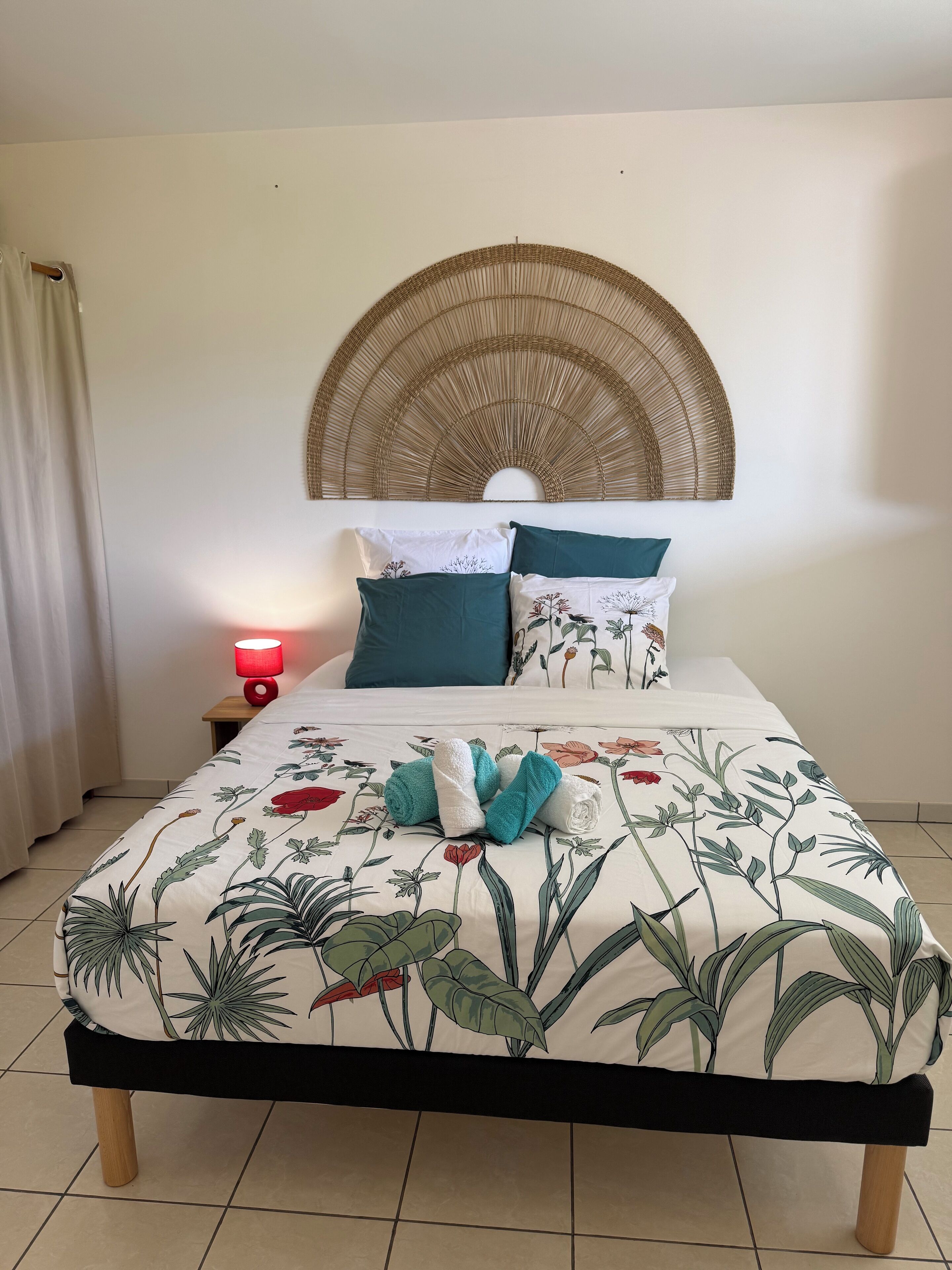 A neatly made bed with floral bedding, a woven headboard, and a bedside lamp.