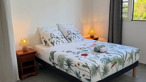 A bedroom with a bed, two bedside tables with lamps, a window with curtains, and an air conditioning unit on the wall. - Alizé Cap (Sainte-Anne)
