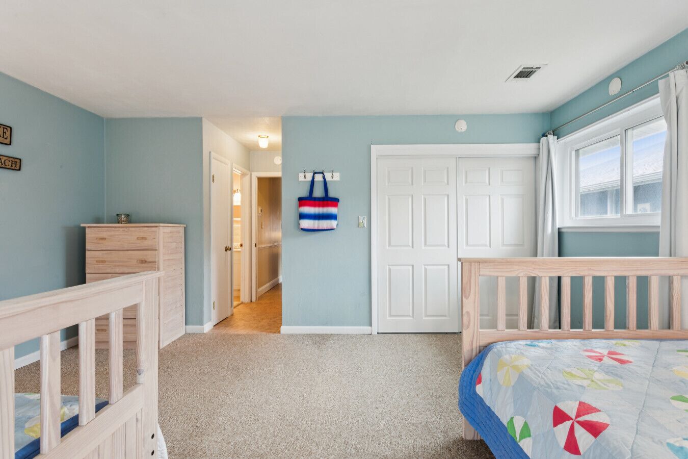 A child's bedroom with a crib, a dresser, and a door leading to another room.