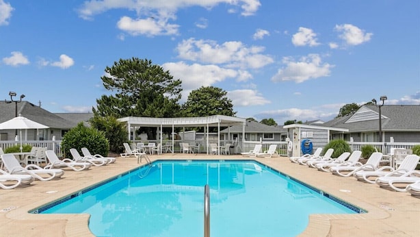 Une piscine rectangulaire à l’eau d’un bleu limpide, entourée de chaises longues blanches et d’un espace de détente abrité.