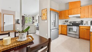 A modern kitchen with wooden cabinets, stainless steel appliances, and a dining area with a table set for two.