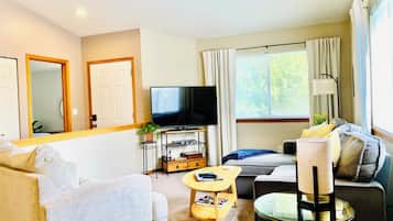 A living room with a sofa, a television, a coffee table, and a window with curtains.