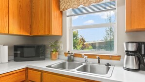 A kitchen with wooden cabinets, a microwave, a sink, a coffee maker, and a window with a view of greenery.