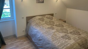 Ein Schlafzimmer mit einem Bett, einem Fenster mit Vorhängen, einem Wandbild und zwei Wandleuchten.